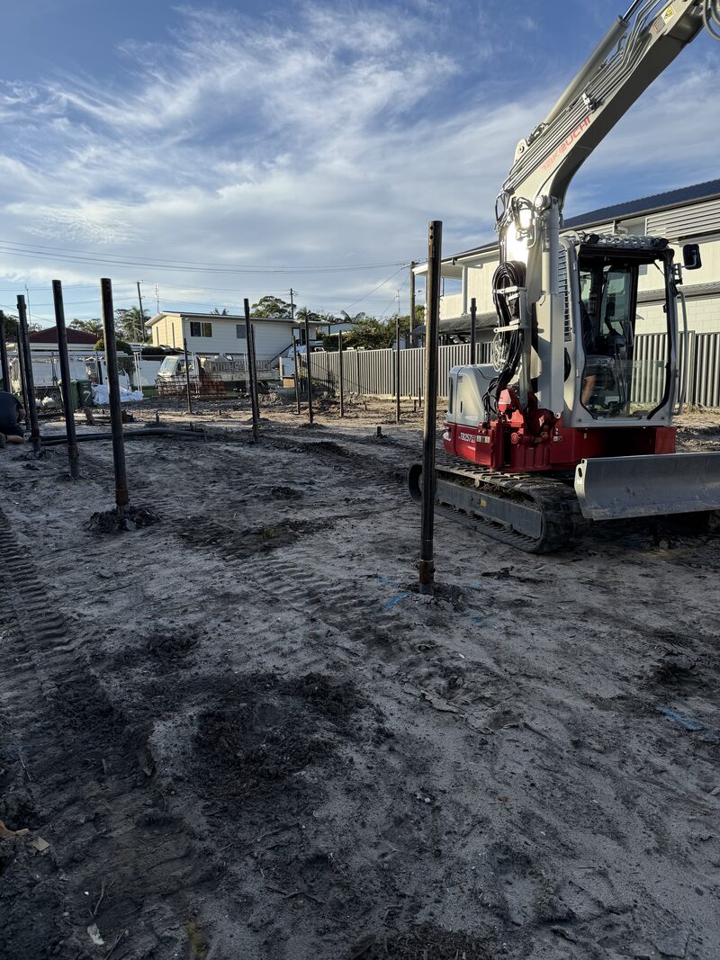 Mini excavator installing steel screw piles across a house site at Mooloolaba